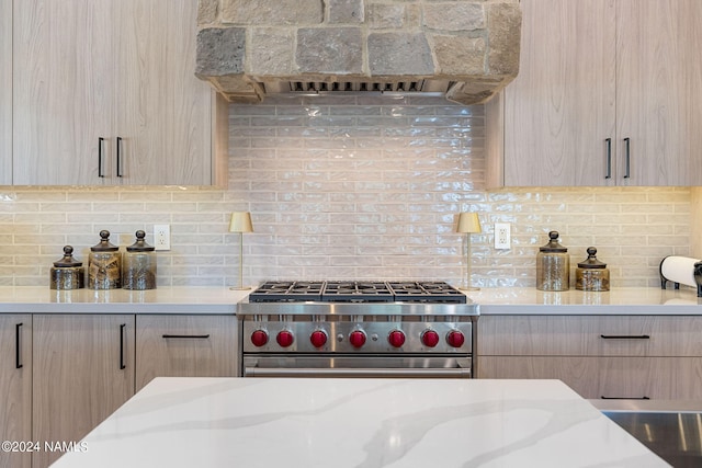 kitchen featuring light brown cabinets, premium range hood, decorative backsplash, and high end range