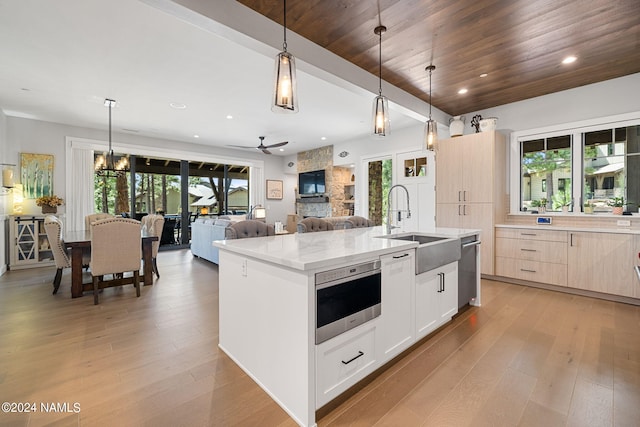 kitchen featuring light stone countertops, white cabinetry, hanging light fixtures, sink, and a center island with sink