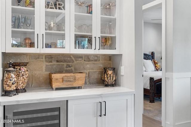 bar featuring wood-type flooring, white cabinetry, beverage cooler, and light stone counters