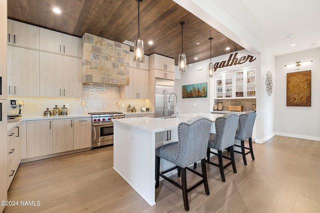 kitchen with premium appliances, tasteful backsplash, custom range hood, and an island with sink