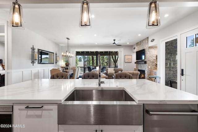 kitchen featuring light stone counters, a center island with sink, pendant lighting, and a fireplace