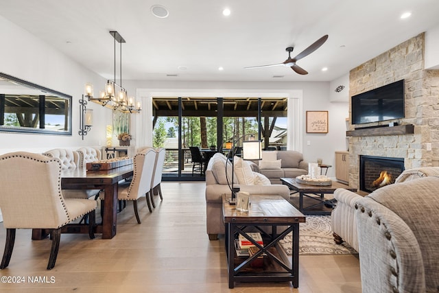 living room with a fireplace, light hardwood / wood-style floors, and ceiling fan with notable chandelier