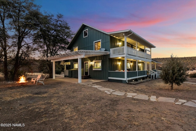 back house at dusk with a fire pit, a hot tub, a patio, and a balcony