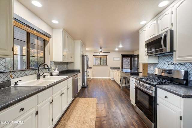 kitchen with sink, ceiling fan, stainless steel appliances, white cabinets, and dark hardwood / wood-style flooring