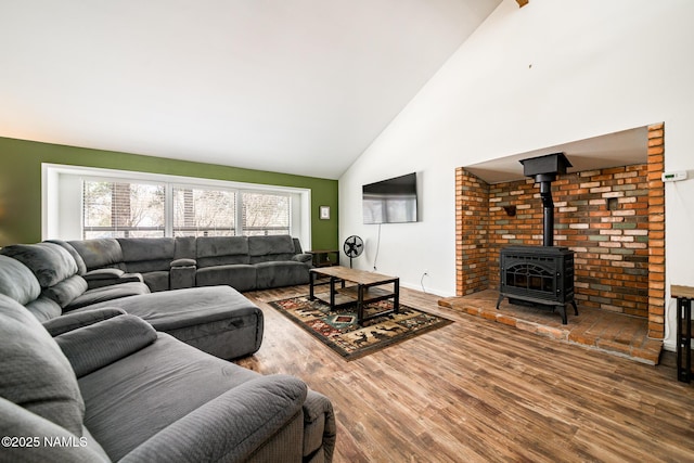living area with high vaulted ceiling, a wood stove, and wood finished floors
