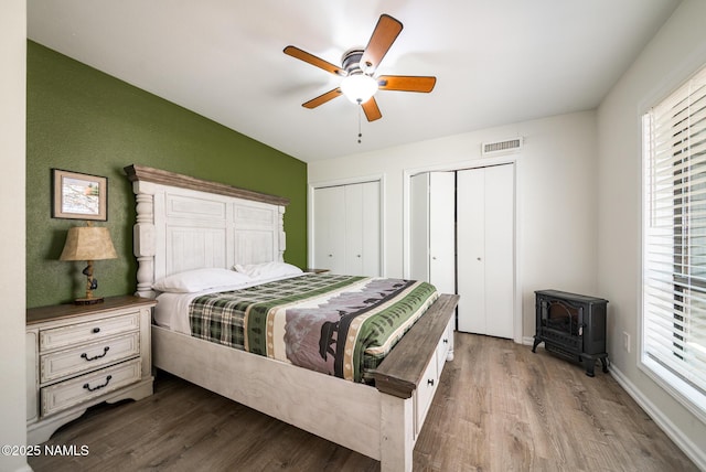 bedroom featuring wood finished floors, a wood stove, visible vents, and multiple closets