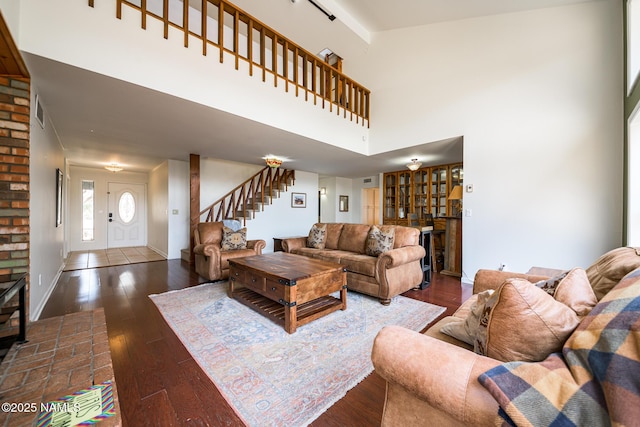 living area with a towering ceiling, dark wood finished floors, visible vents, and stairs