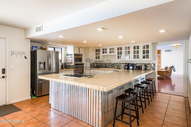 kitchen featuring light tile patterned floors, visible vents, appliances with stainless steel finishes, a peninsula, and tile countertops