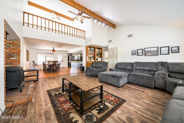 living room featuring a wood stove, ceiling fan, high vaulted ceiling, wood finished floors, and beam ceiling