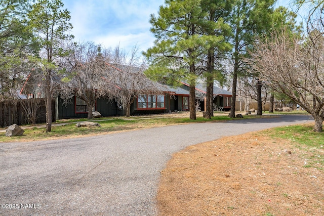 view of front facade with board and batten siding, aphalt driveway, and fence
