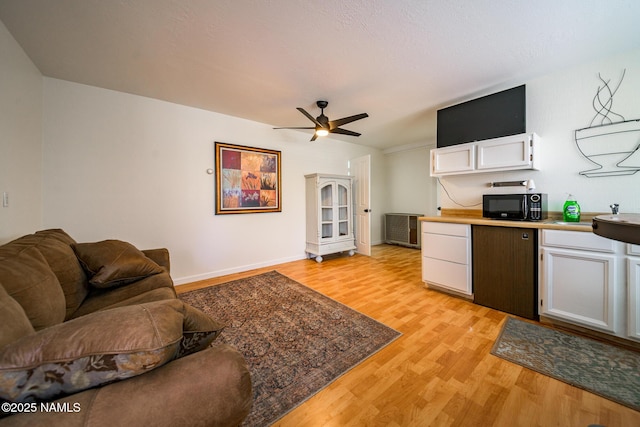living area with light wood-style floors, baseboards, and a ceiling fan