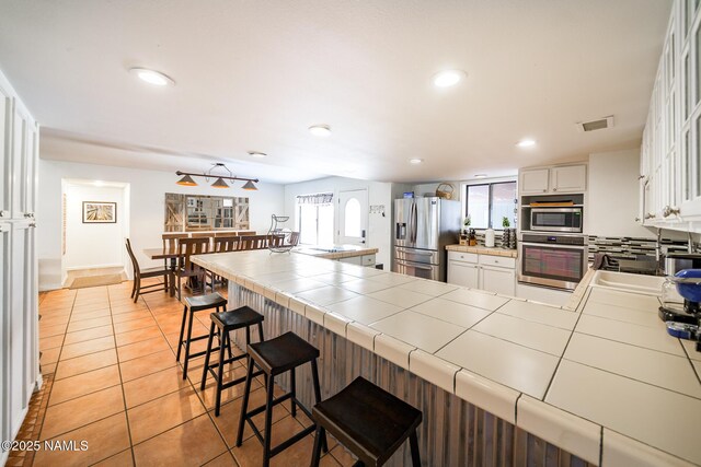 kitchen with recessed lighting, visible vents, stainless steel appliances, tile countertops, and a sink