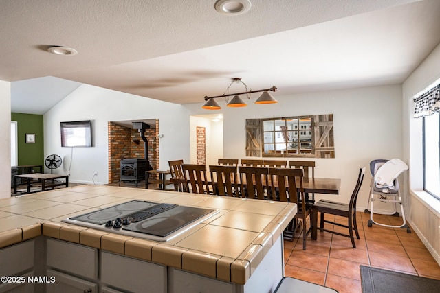 kitchen with a wood stove, light tile patterned floors, lofted ceiling, tile counters, and black electric cooktop
