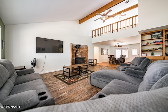 living area with a wood stove, ceiling fan, wood finished floors, baseboards, and beam ceiling
