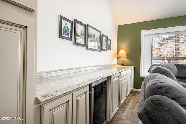 bar with vaulted ceiling, a bar, dark wood-style flooring, wine cooler, and baseboards