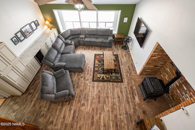 living room featuring a wood stove, a ceiling fan, and wood finished floors