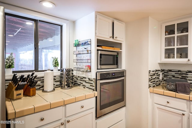 kitchen with backsplash, white cabinets, tile countertops, and stainless steel appliances
