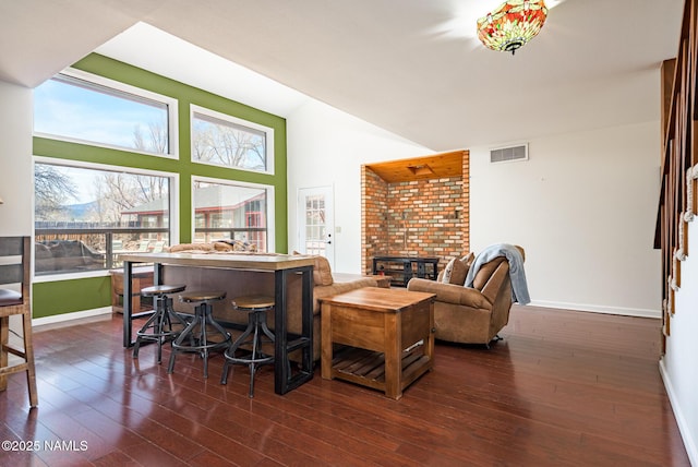 living area with high vaulted ceiling, dark wood finished floors, visible vents, a brick fireplace, and baseboards