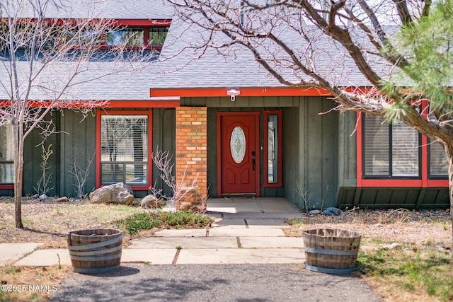 property entrance featuring brick siding, board and batten siding, and roof with shingles