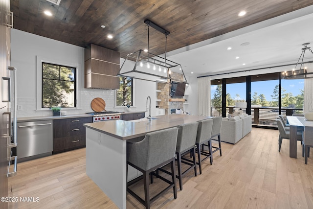 kitchen featuring extractor fan, an inviting chandelier, pendant lighting, stainless steel appliances, and a kitchen island with sink