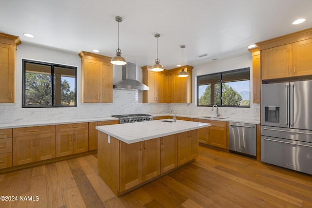 kitchen featuring appliances with stainless steel finishes, wall chimney exhaust hood, sink, light stone counters, and a center island with sink