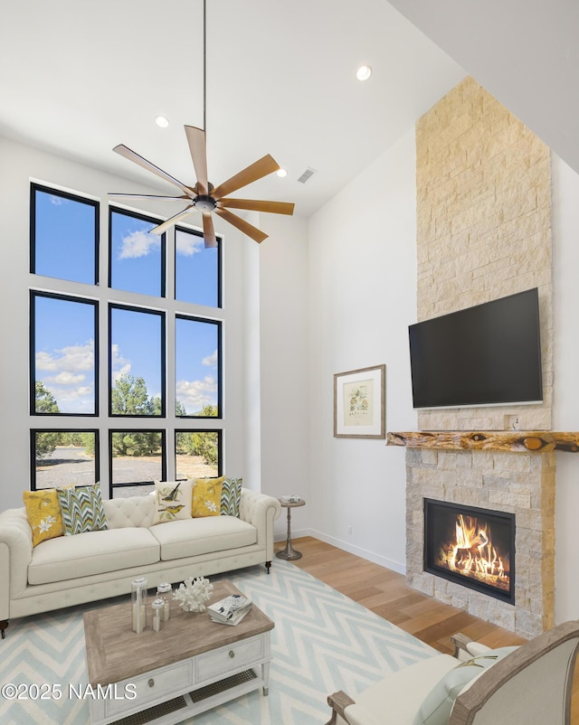 living area with a ceiling fan, a high ceiling, a fireplace, light wood finished floors, and baseboards