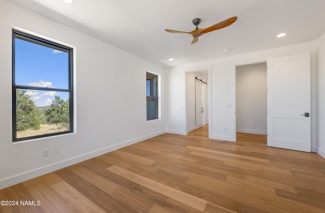 unfurnished bedroom featuring light hardwood / wood-style floors, ceiling fan, and a barn door