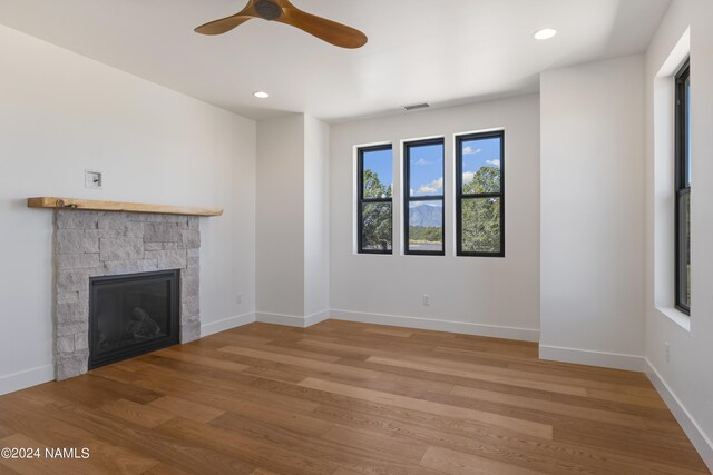 unfurnished living room with light wood-type flooring, ceiling fan, and a stone fireplace