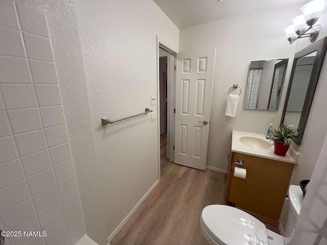 half bath with wood finished floors, a textured wall, toilet, vanity, and baseboards