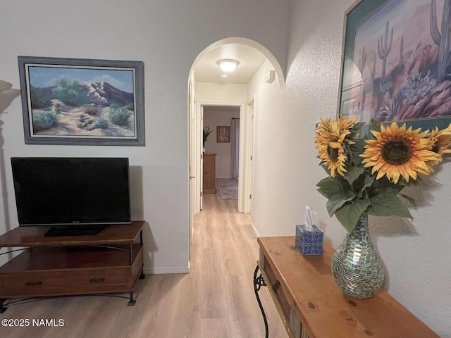 corridor featuring arched walkways, light wood-style floors, and baseboards