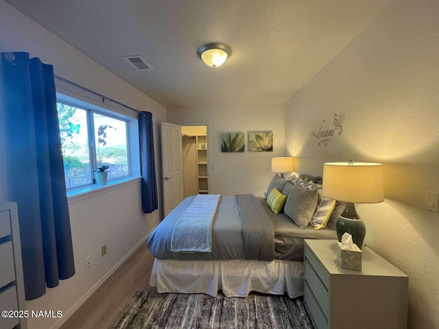 bedroom with a walk in closet, wood finished floors, visible vents, and baseboards