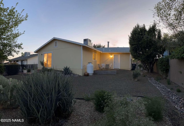 back of house at dusk featuring stucco siding and fence