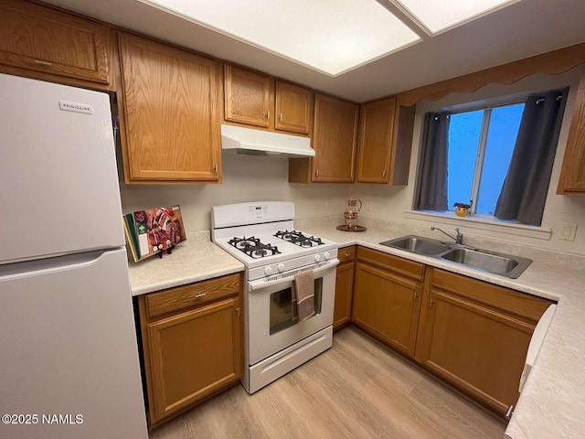 kitchen featuring light wood finished floors, a sink, white appliances, light countertops, and under cabinet range hood