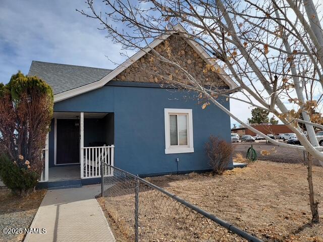 exterior space with a shingled roof, covered porch, fence, and stucco siding