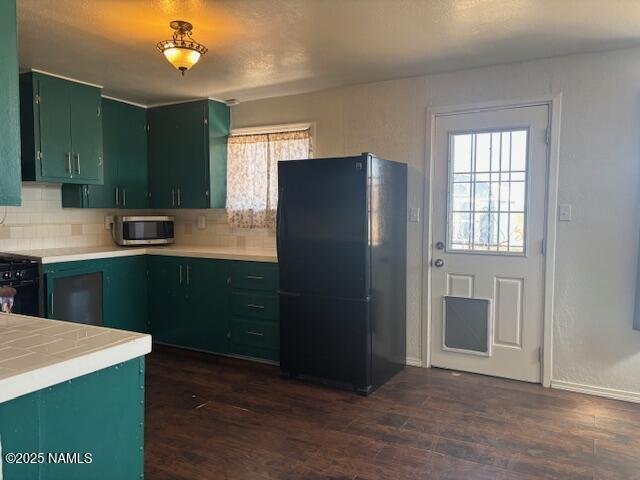 kitchen featuring black appliances, dark wood-style floors, green cabinets, and decorative backsplash