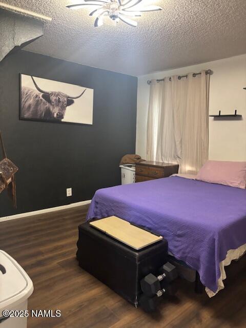 bedroom featuring a ceiling fan, a textured ceiling, baseboards, and wood finished floors