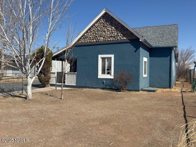 view of side of property featuring a shingled roof, fence, and stucco siding