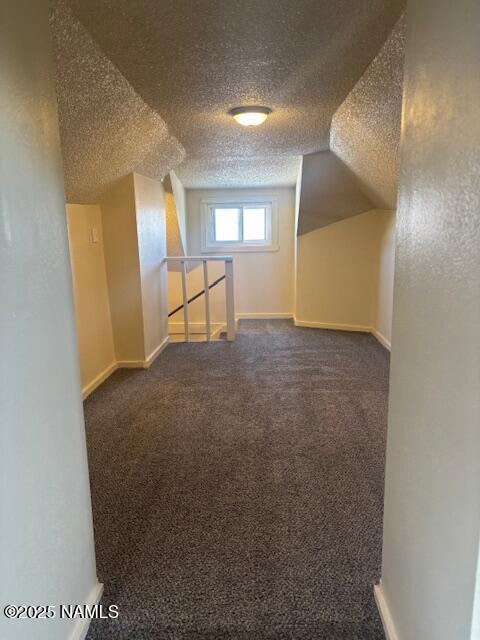 bonus room with lofted ceiling, baseboards, dark colored carpet, and a textured ceiling