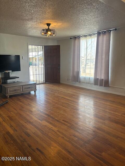 unfurnished living room featuring a textured ceiling, baseboards, and wood finished floors