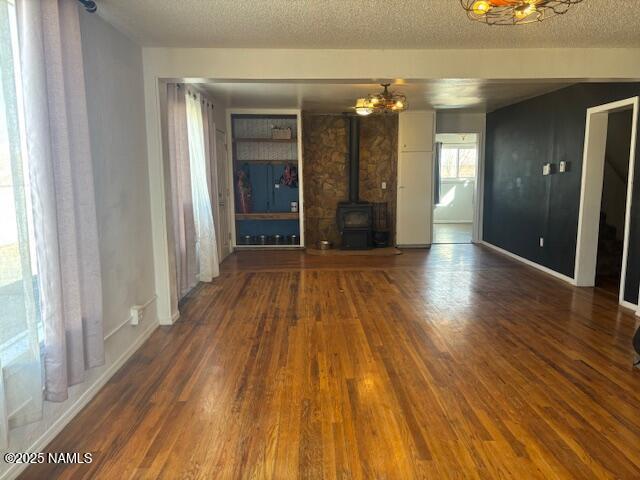 unfurnished living room with a textured ceiling, wood finished floors, a wood stove, and baseboards