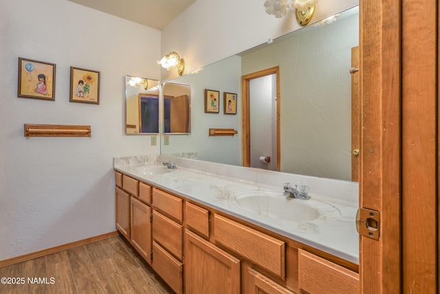 full bath with double vanity, a sink, baseboards, and wood finished floors