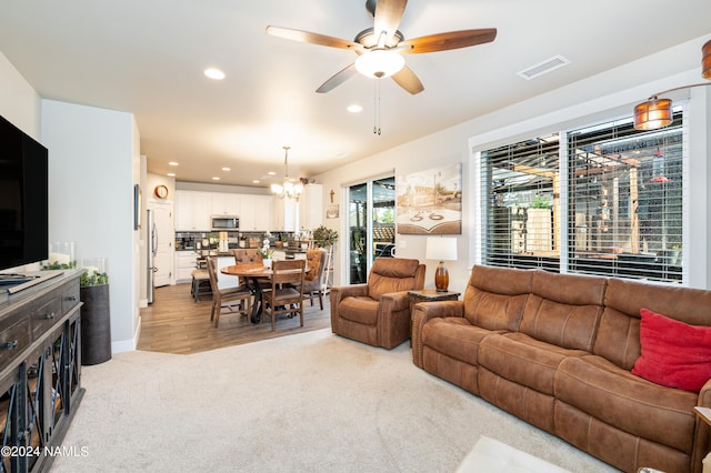 carpeted living room featuring ceiling fan with notable chandelier