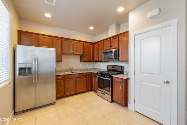 kitchen with light stone counters, stainless steel appliances, sink, and light tile patterned floors