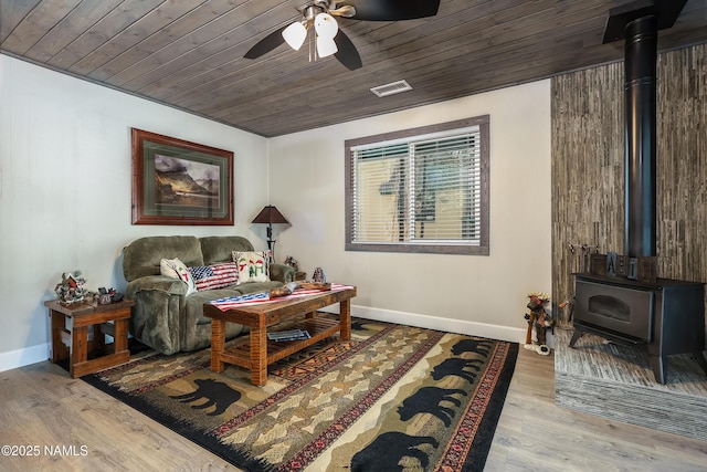 living room with wooden ceiling, a wood stove, baseboards, and wood finished floors