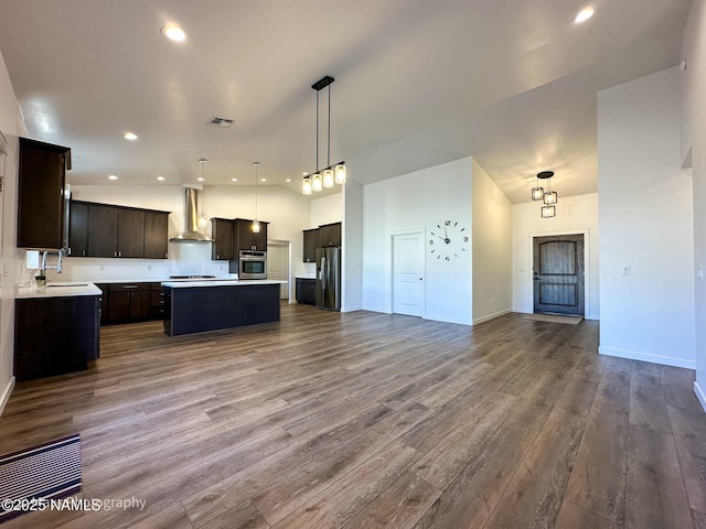 kitchen with appliances with stainless steel finishes, open floor plan, dark wood-type flooring, wall chimney range hood, and a sink