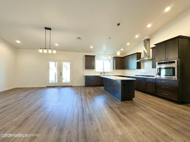 kitchen featuring wall chimney exhaust hood, a kitchen island, wood finished floors, french doors, and stainless steel oven