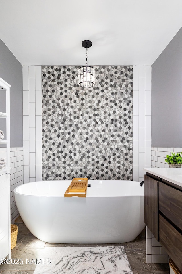 full bath with a freestanding bath, vanity, and tile walls