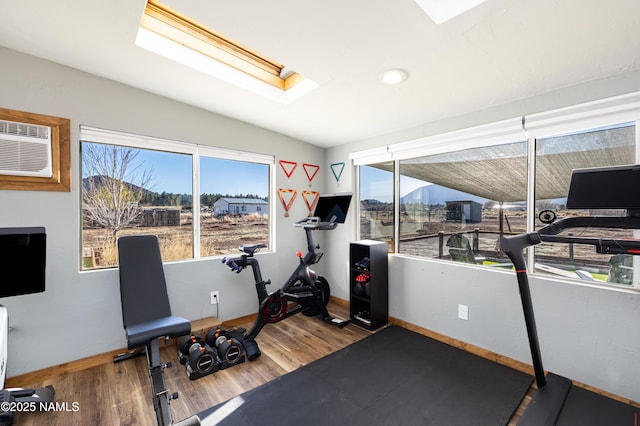 exercise area with an AC wall unit, baseboards, wood finished floors, and a skylight
