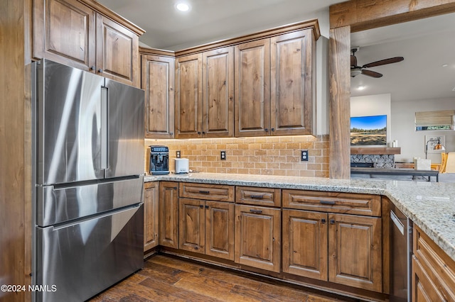 kitchen with light stone countertops, dark wood-type flooring, decorative backsplash, stainless steel fridge, and ceiling fan