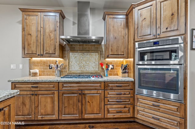 kitchen featuring backsplash, light stone counters, wall chimney exhaust hood, and appliances with stainless steel finishes